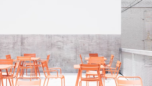 Orange tables and chairs  in front of a concrete wall